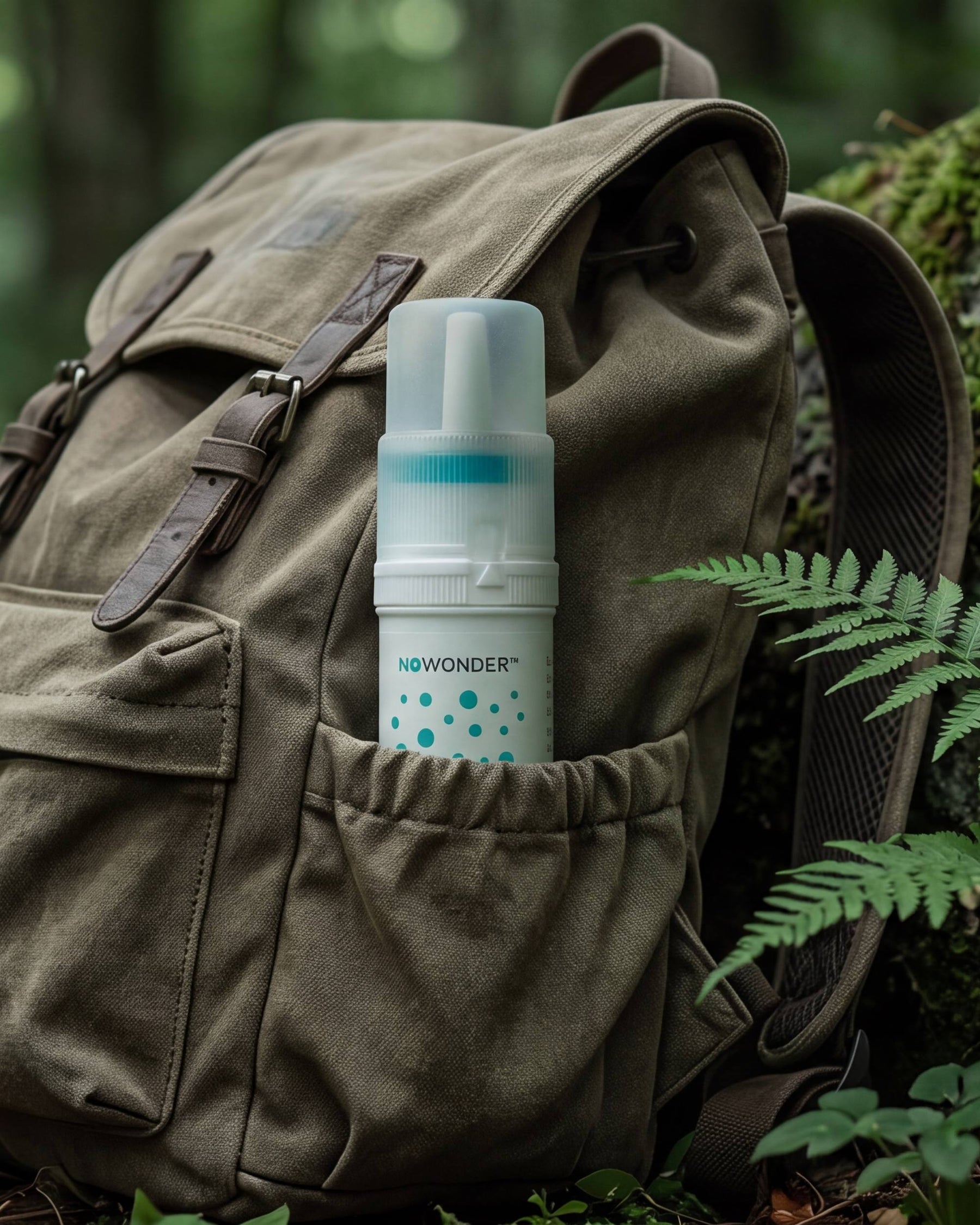 A bottle of NOWONDER Nasal Cleanser  tucked into the front pocket of a backpack, set against a lush green forest background.